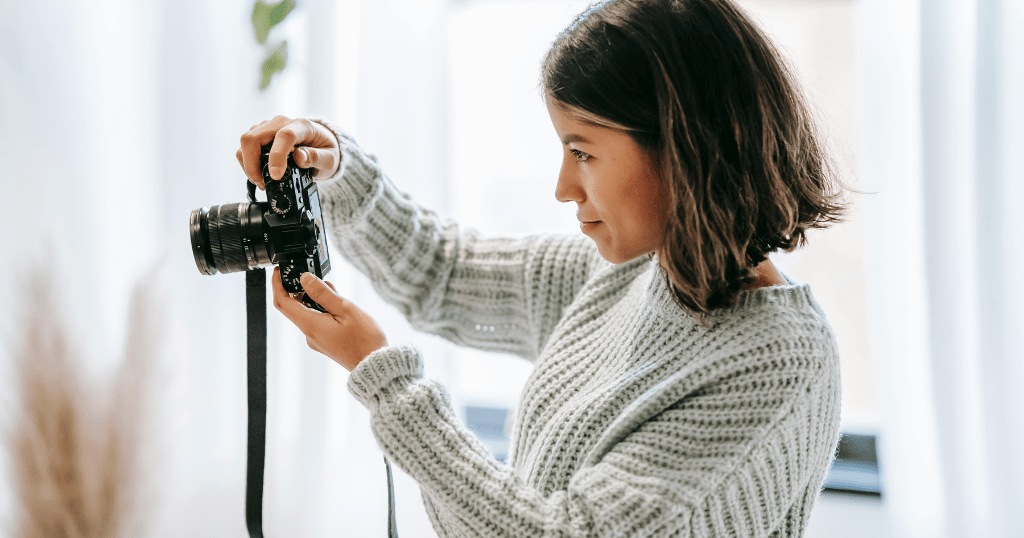 Mulher de cabelo curto segurando uma câmera enquanto sorri tirando uma fotografia