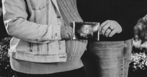 Casal abraçado, segurando fotografia de ultrassom do bebê. A foto está em preto e branco.