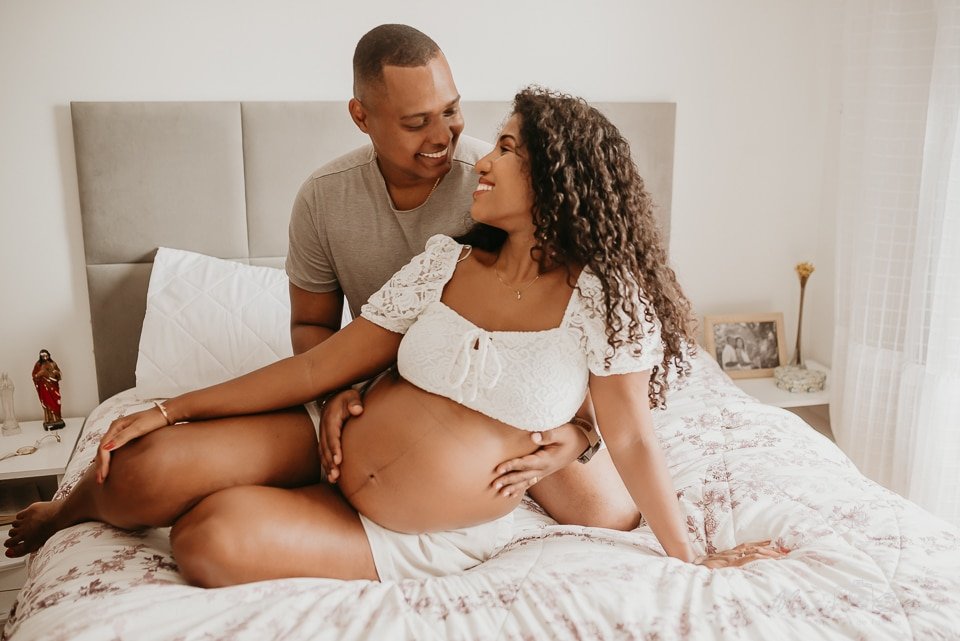 Casal eternizando gravidez em fotografia. Os dois estão abraçados, com a mão na barriga da mãe.