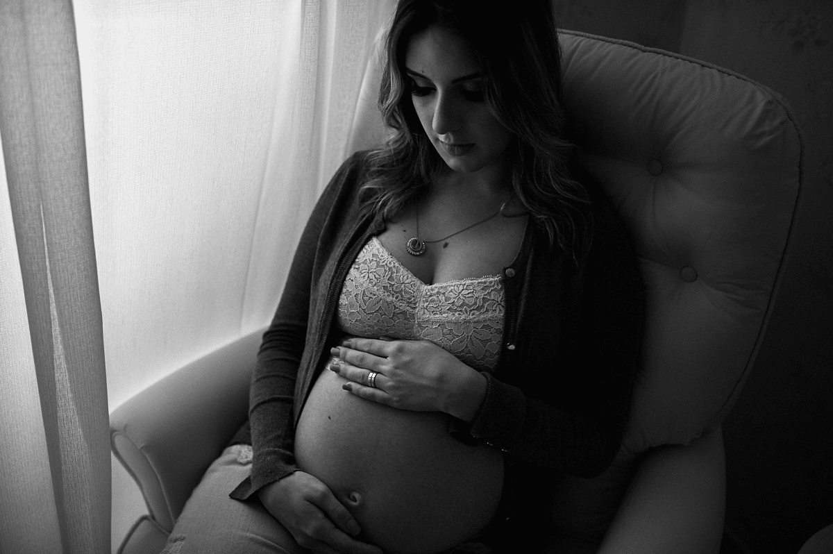 Mulher grávida sentada, com mãos na barriga. É uma foto preto e branco