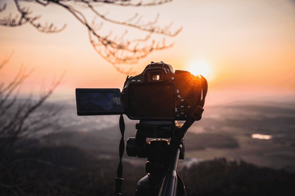 câmera em um tripé no alto de uma serra fotografando o pôr do sol 