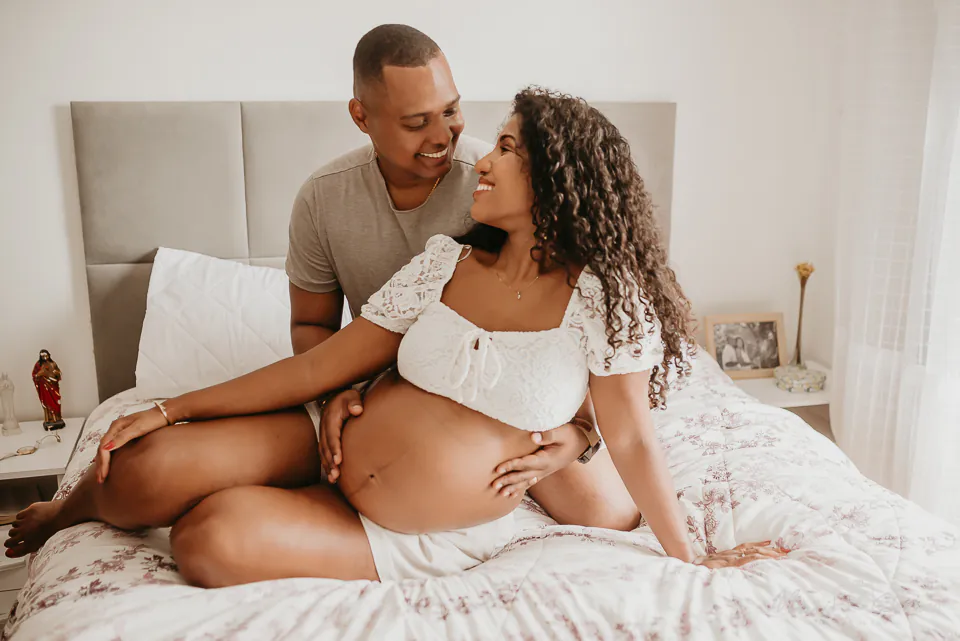 foto-de-gestante-estilo-lifestyle Casal eternizando gravidez em fotografia. Os dois estão abraçados, com a mão na barriga da mãe.
