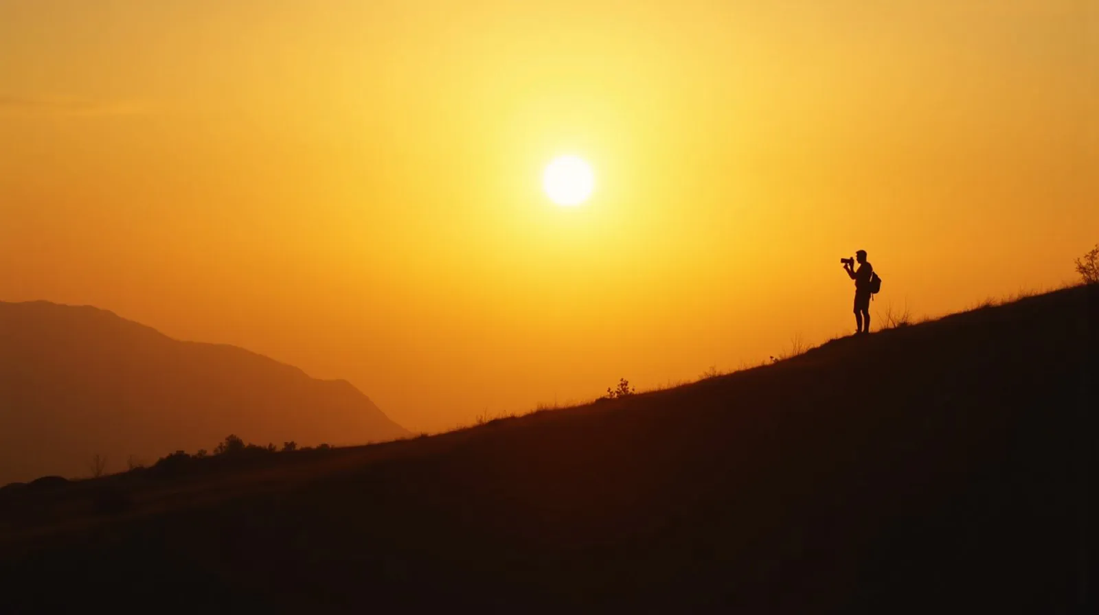Silhueta de fotógrafo em uma colina fotografando o pôr do sol, com a câmera erguida contra a luz dourada do entardecer